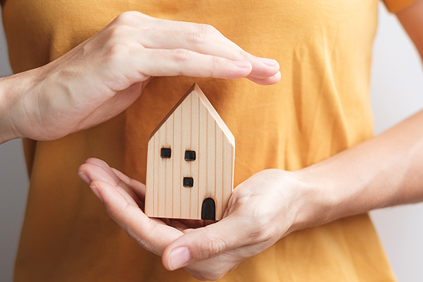 Mãos protegendo uma casa em miniatura, simbolizando cuidado e proteção